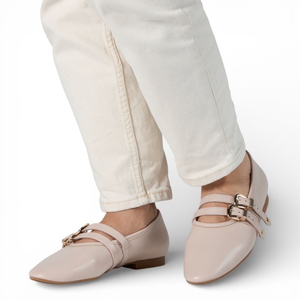 Dover Bone Leather Flat with Double Strap Detail shoes with gold buckles worn with white pants on a light gray background